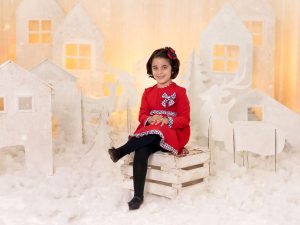 reportaje de fotos de navidad a niña vestido rojo en estudio en Murcia con decorado navideño de siluetas de renos, pinos, casa nórdicas