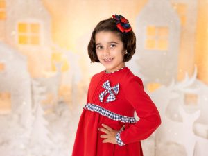 reportaje de fotos de navidad a niña vestido rojo en estudio en Murcia con decorado navideño de siluetas de renos, pinos, casa nórdicas
