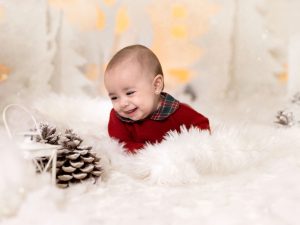 sesión de fotos de navidad a bebe en estudio traje rojo en Murcia con decorado navideño de siluetas de renos, pinos, casa nórdicas