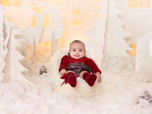 sesión de fotos de navidad a bebe en estudio traje rojo en Murcia con decorado navideño de siluetas de renos, pinos, casa nórdicas