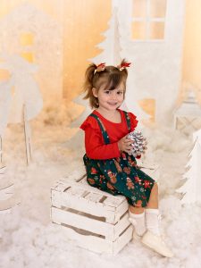 sesión de fotos de navidad a peques en estudio traje rojo en Murcia con decorado navideño de siluetas de renos, pinos, casa nórdicas