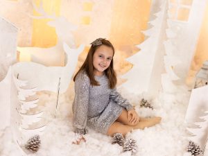 sesión de fotos de navidad a peques en estudio vestido plata de brillo fiesta nochevieja navideño en Murcia con decorado navideño de siluetas de renos, pinos, casa nórdicas