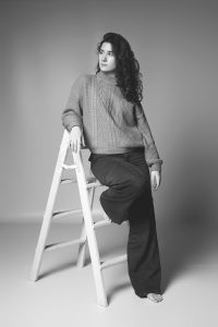 sesión fotos de estudio en blanco y negro con outfit casual apoyada en escalera con poses naturales